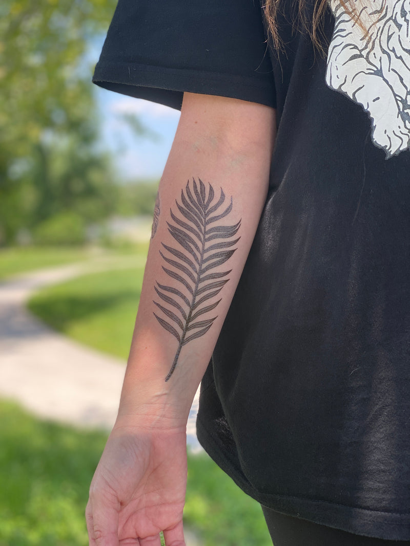 palm leaf temporary tattoo on persons arm wearing black in a blurred nature background 