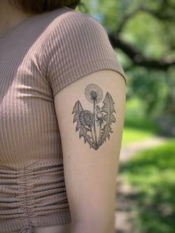 A photo of a person's arm with a temporary tattoo of a blooming dandelion plant design.