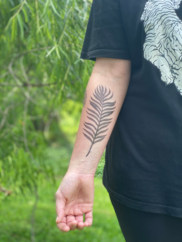palm leaf temporary tattoo on persons arm wearing black and white in a green nature background 