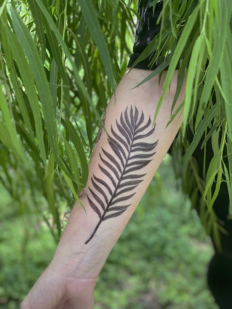 palm leaf temporary tattoo on persons arm wearing black in a green nature background 