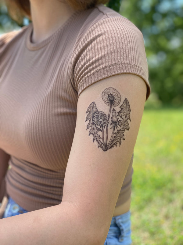 Dandelion temporary tattoo on upper arm with blurred nature background 
