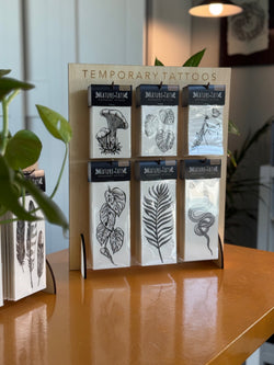 Sets of temporary tattoo packages on a wooden stand with a plant in the background