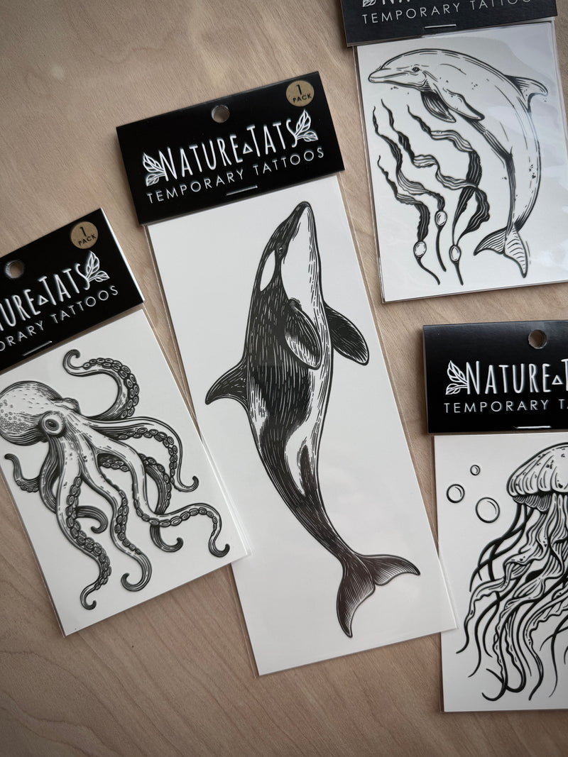 Nature-Tats temporary tattoos with whale, octopus, and jellyfish designs on a wooden surface.