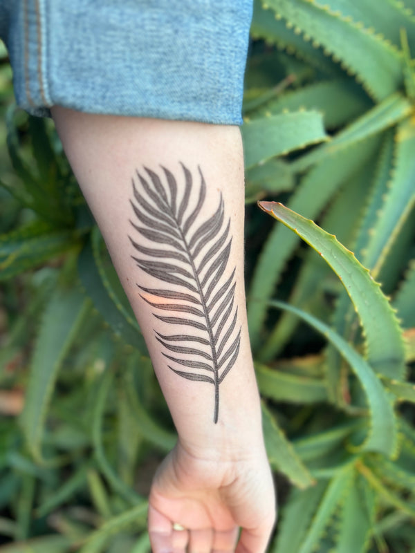 palm leaf temporary tattoo on persons arm wearing blue in a green nature background 