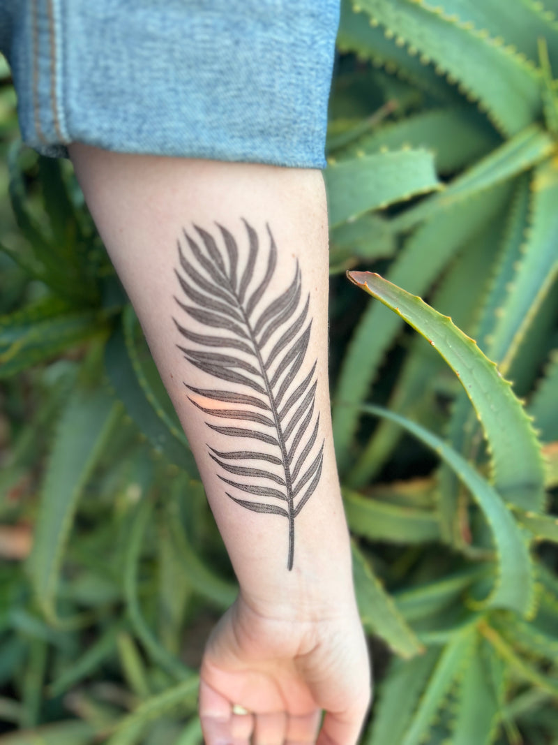 palm leaf temporary tattoo on persons arm wearing blue in a green nature background 