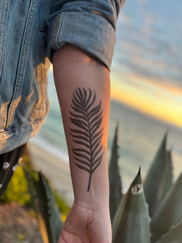 palm leaf temporary tattoo on persons arm wearing blue and black in a blurred nature background 