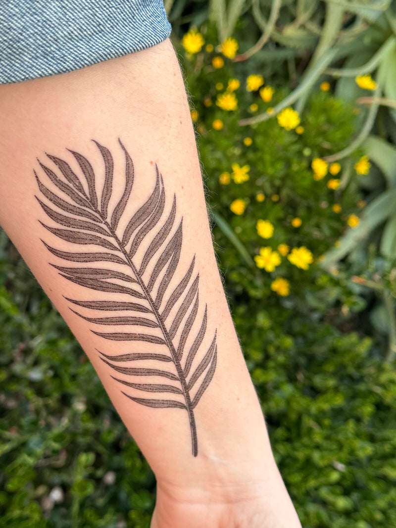 palm leaf temporary tattoo on persons arm wearing blue in a nature background 