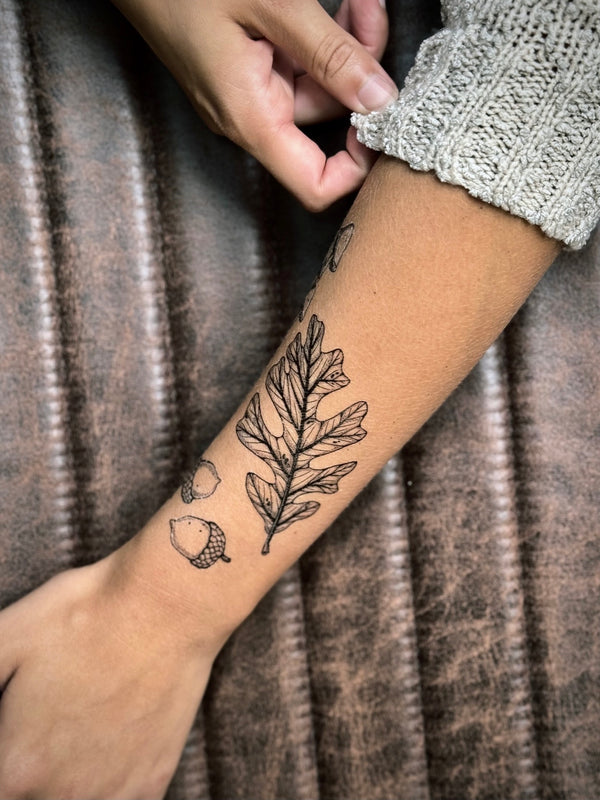 Temporary Tattoo of a leaf and acorn design on a person's arm with a textured brown background.