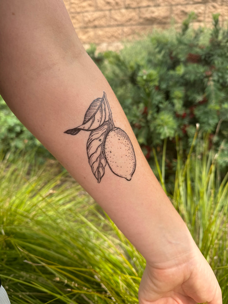 lemon with leaves temporary tattoo on persons arm in a green nature background 