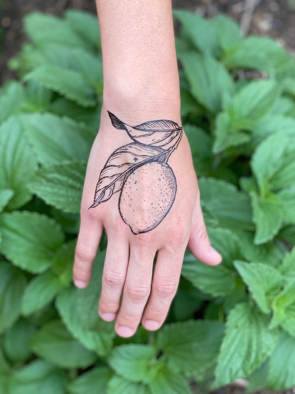 lemon with leaves temporary tattoo on person hand in a green nature background 