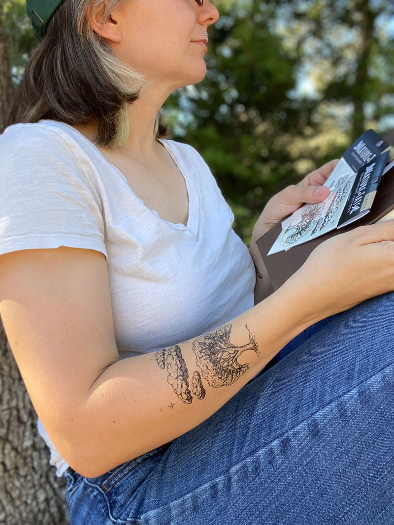 Live Oak Sky temporary tattoo on persons arm wearing white and blue jeans in a blurred nature background 