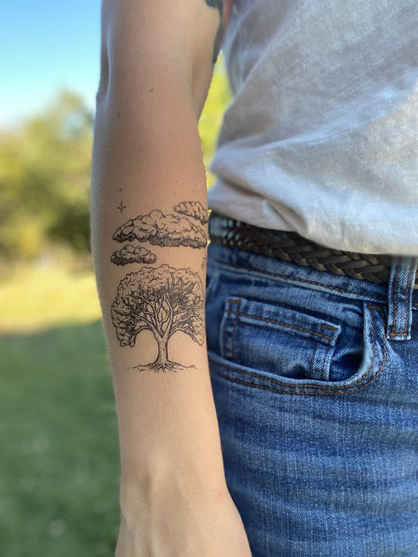 Live Oak Sky temporary tattoo on persons arm wearing white and blue jeans in blurred nature background 