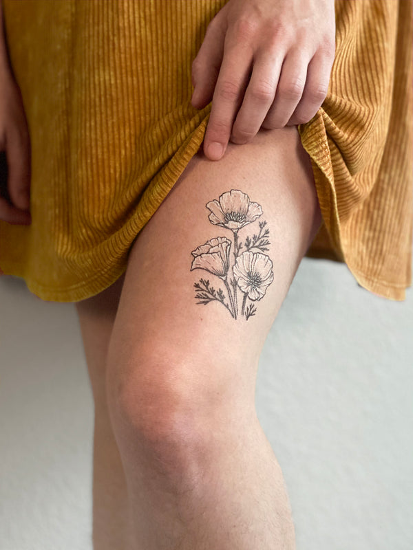 golden poppy temporary tattoo on persons leg wearing a orange dress with a white background 