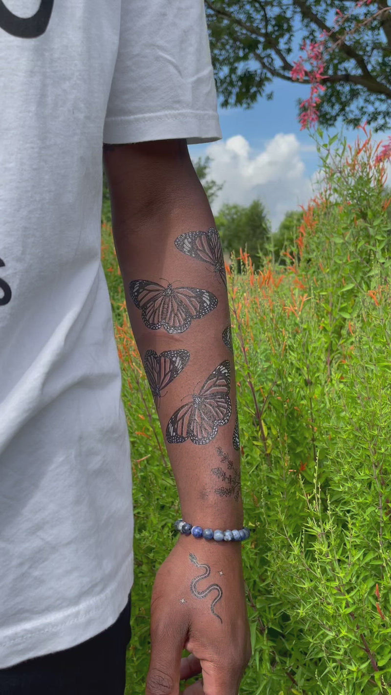 Monarch Butterfly temporary tattoo on persons arm wearing white with a green nature background 