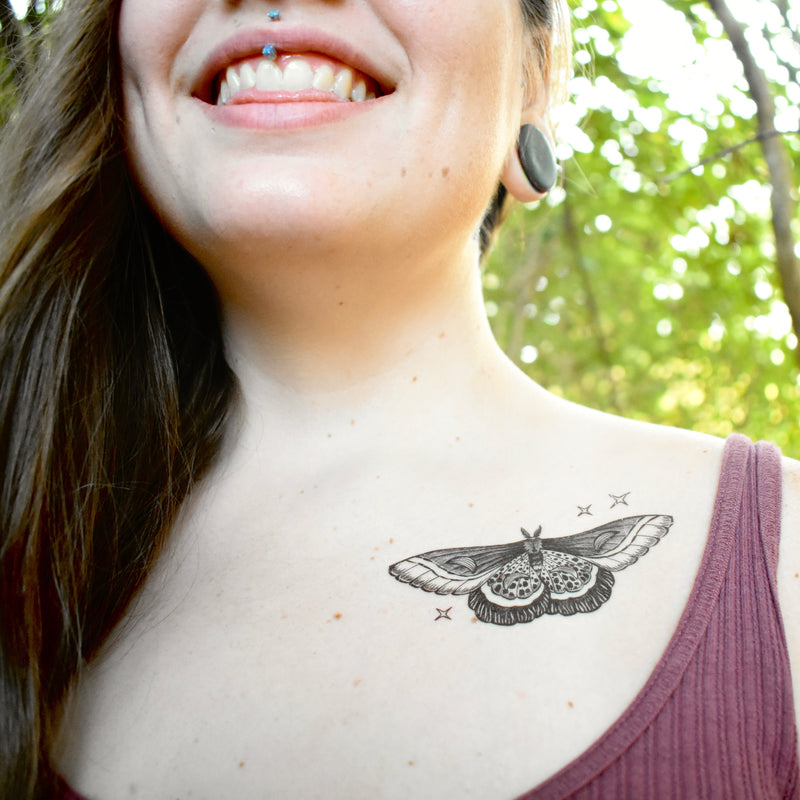 night moth temporary tattoo with stars on persons collarbone wearing dark red in a blurred nature background 