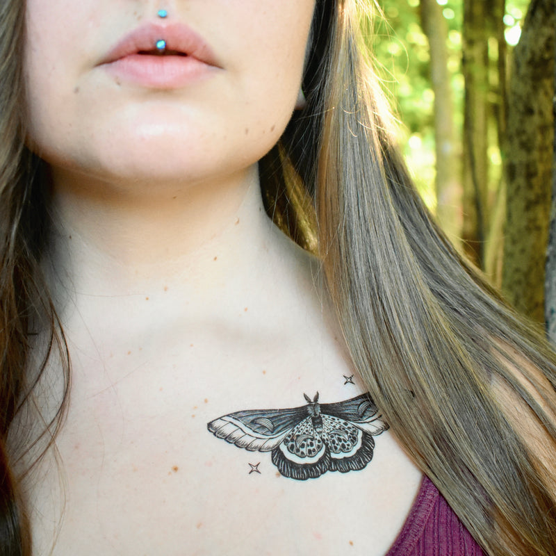 night moth temporary tattoo with stars on persons collarbone with brown hair in blurred nature background 