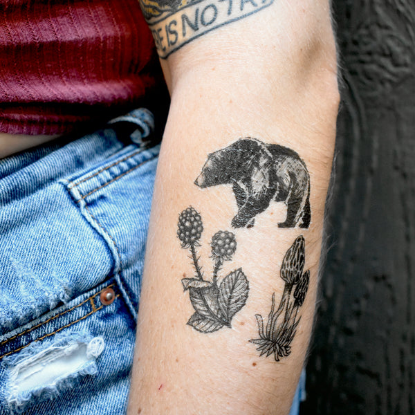 forest forage temporary tattoo on person below elbow wearing red shirt and blue jeans with a dark brown background 