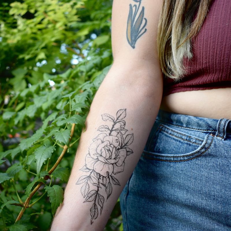 Rose temporary tattoo on persons arm wearing red and blue in a green nature background 
