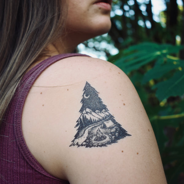 mountain camping temporary tattoo on persons shoulder wearing dark red in a green nature background 