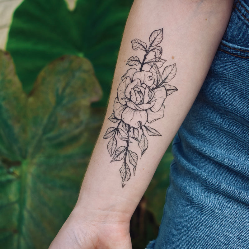 Rose temporary tattoo on persons arm wearing blue in a green nature background 