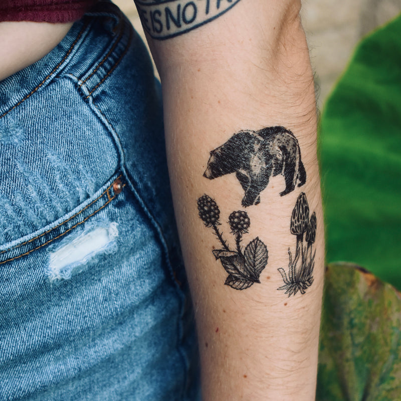 forest forage temporary tattoo below elbow on person wearing blue jeans with a  green background 
