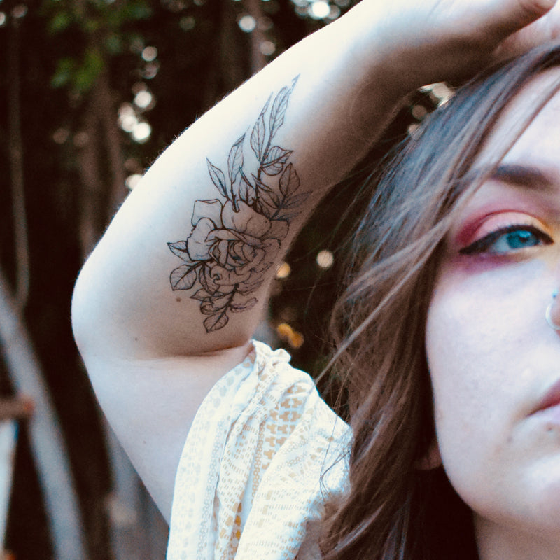 rose temporary tattoo on persons arm wearing white in a blurred brown background 