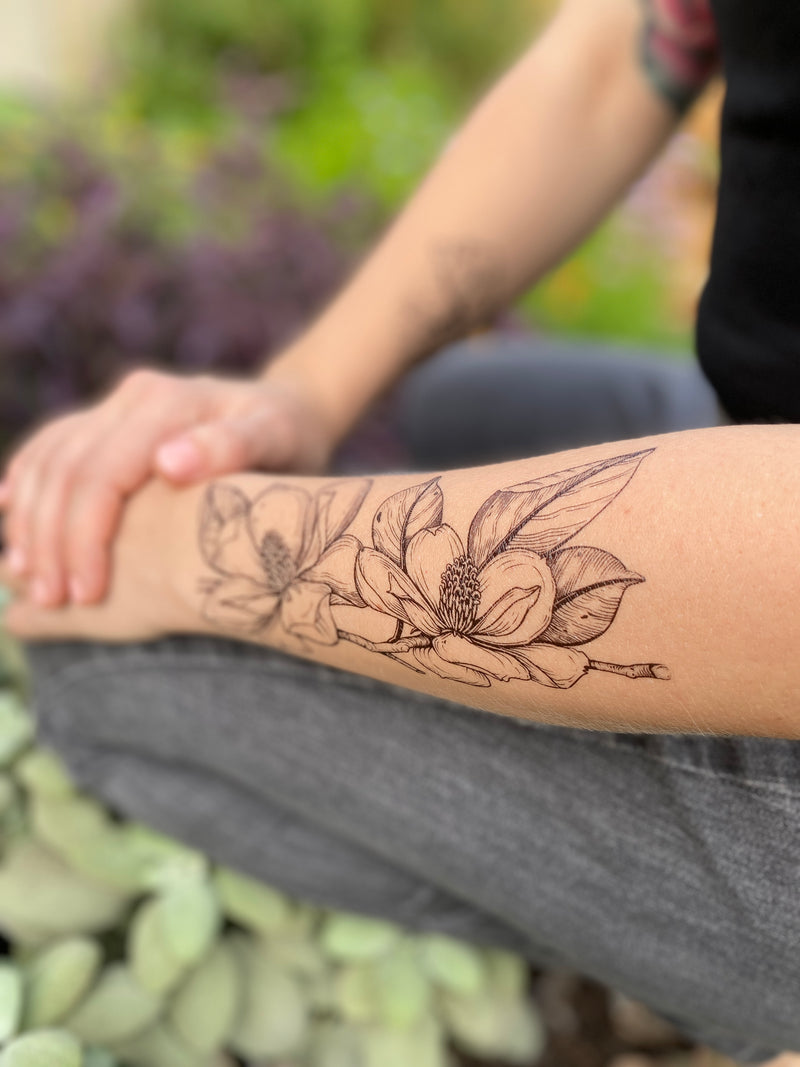magnolia flowers on persons arm wearing grey and black in a blurred nature background 