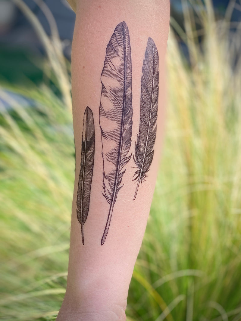 feather finds temporary tattoo on leg with a green leaf background 