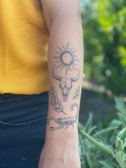 Temporary tattoos on a person's arm featuring a sun, a bull skull, and other designs related to the American Southwest.