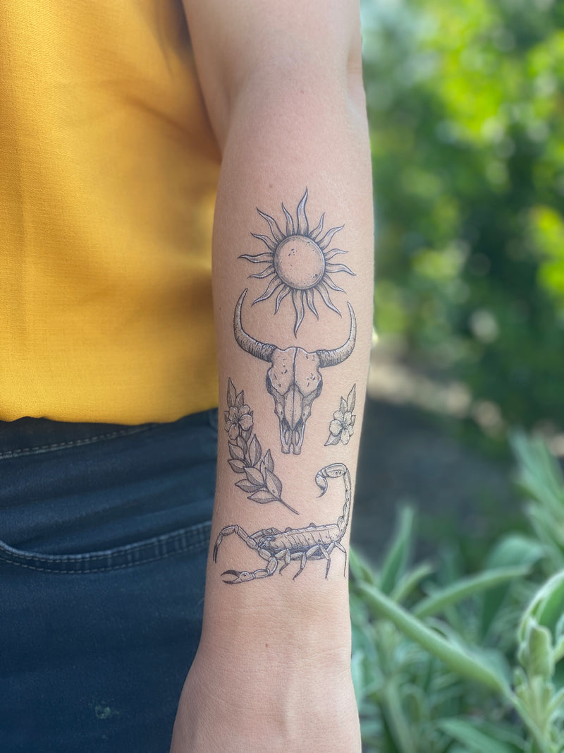 Temporary tattoos on a person's arm featuring a sun, a bull skull, and other designs related to the American Southwest.