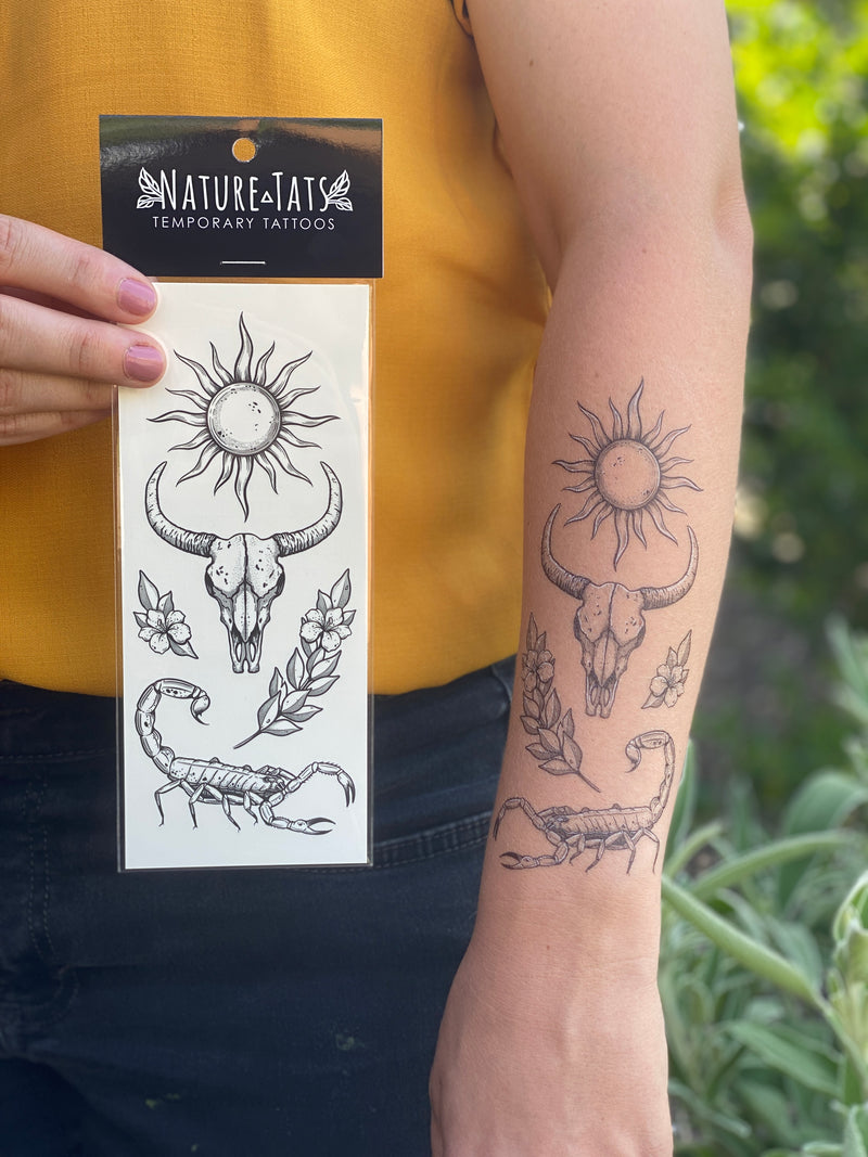 sunlit south temporary tattoo collection on persons arm with one also in it packaging, with a person wearing yellow and blue in a blurred nature background 