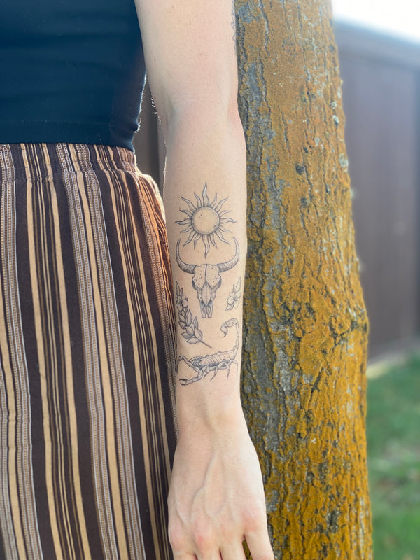 sunlit south temporary tattoo collection on persons arm wearing brown and black in a blurred nature background 