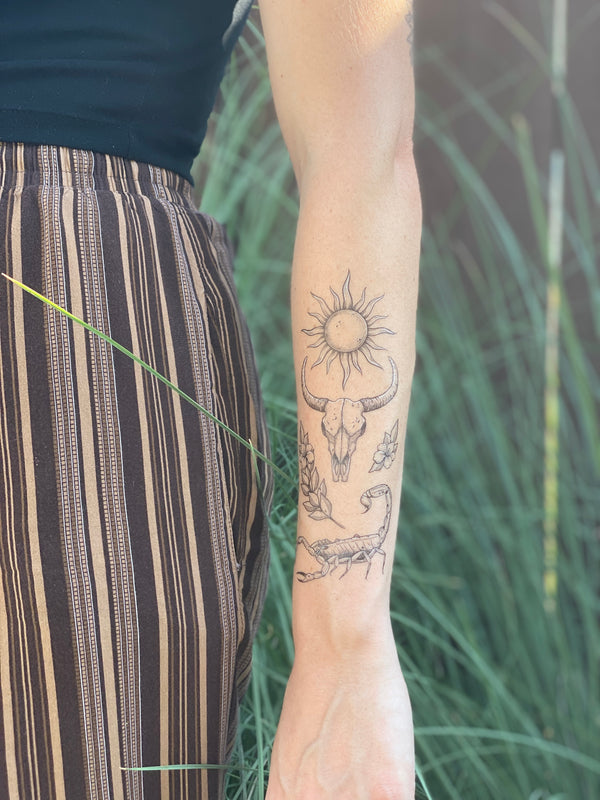 sunlit south temporary tattoo collection on persons arm wearing brown and black in a blurred nature background 