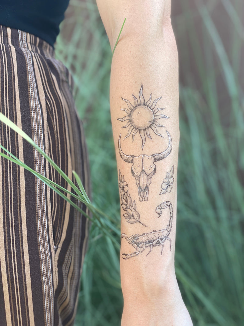 sunlit south temporary tattoo collection on persons arm wearing black and brown in a blurred nature background 