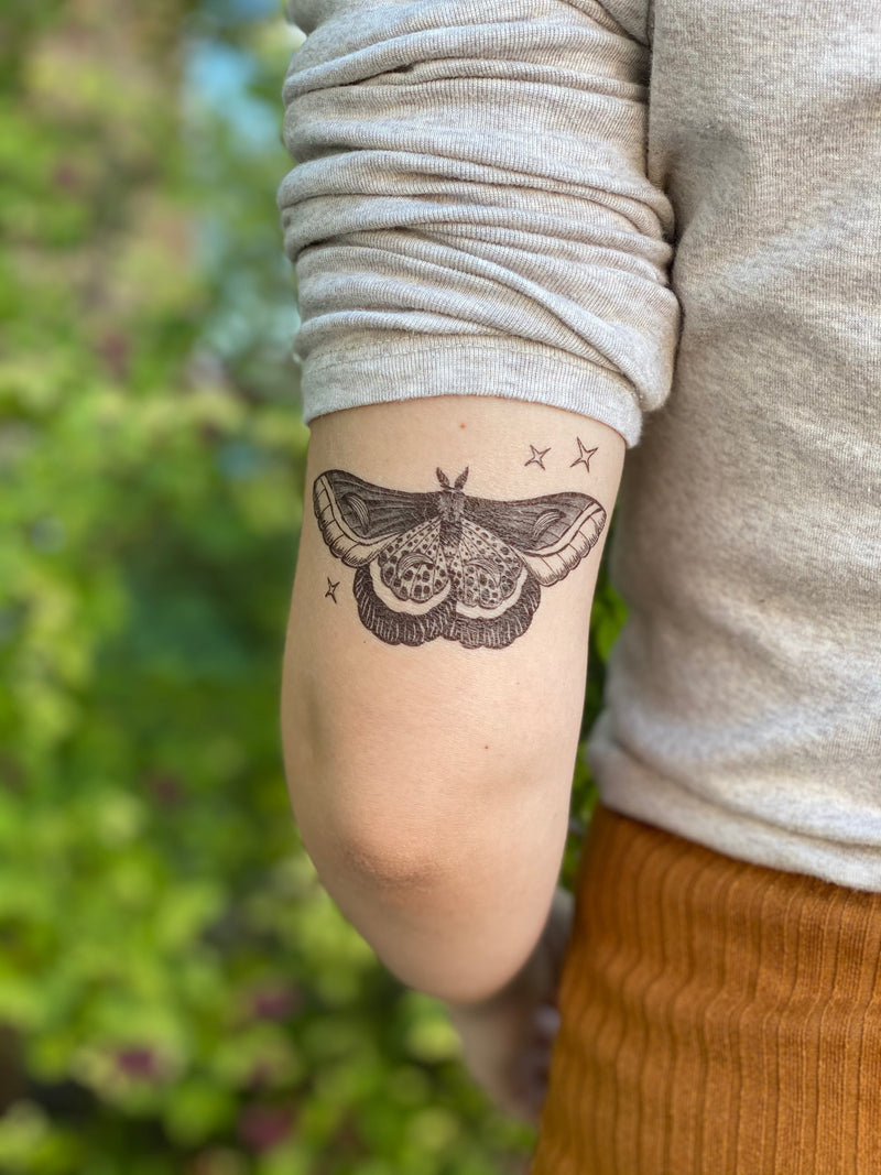 night moth temporary tattoo with stars on the back of persons arm in a blurred green background 