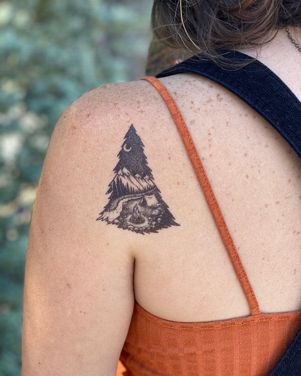 mountain camping temporary tattoo on persons shoulder wearing orange and black in a blurred nature background 
