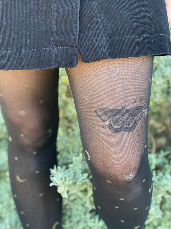 night moth temporary tattoo with stars on persons leg wearing black in a green nature background 