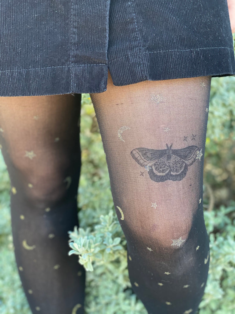 night moth temporary tattoo with stars on persons leg wearing black in a green nature background 