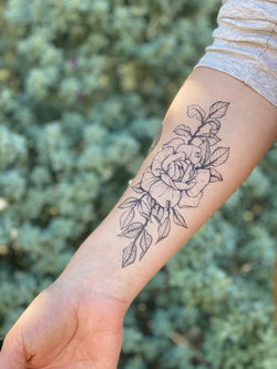 A hand with a temporary tattoo of a rose blossom design, applied on the forearm.