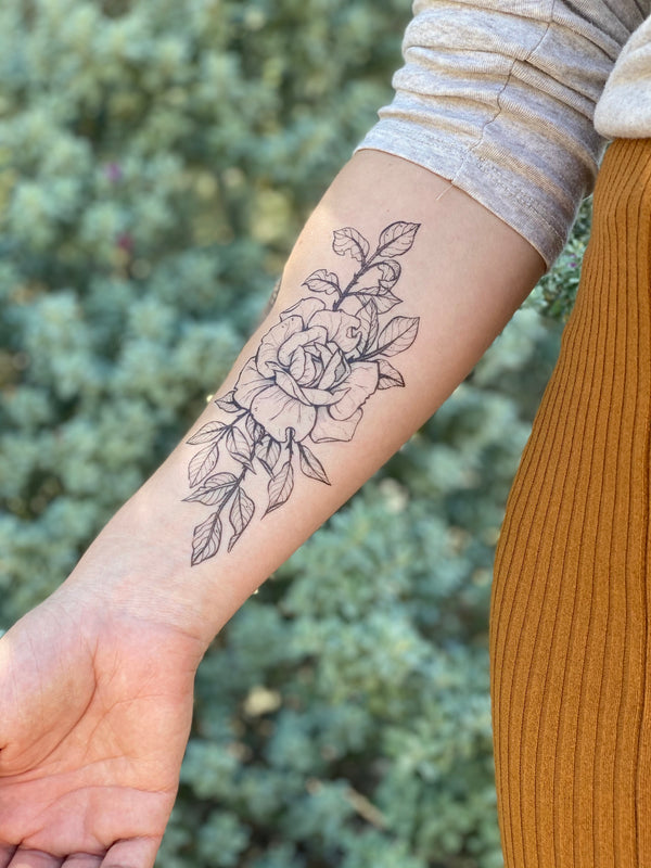 Rose temporary tattoo on persons arm wearing orange and white in a green blurred background 