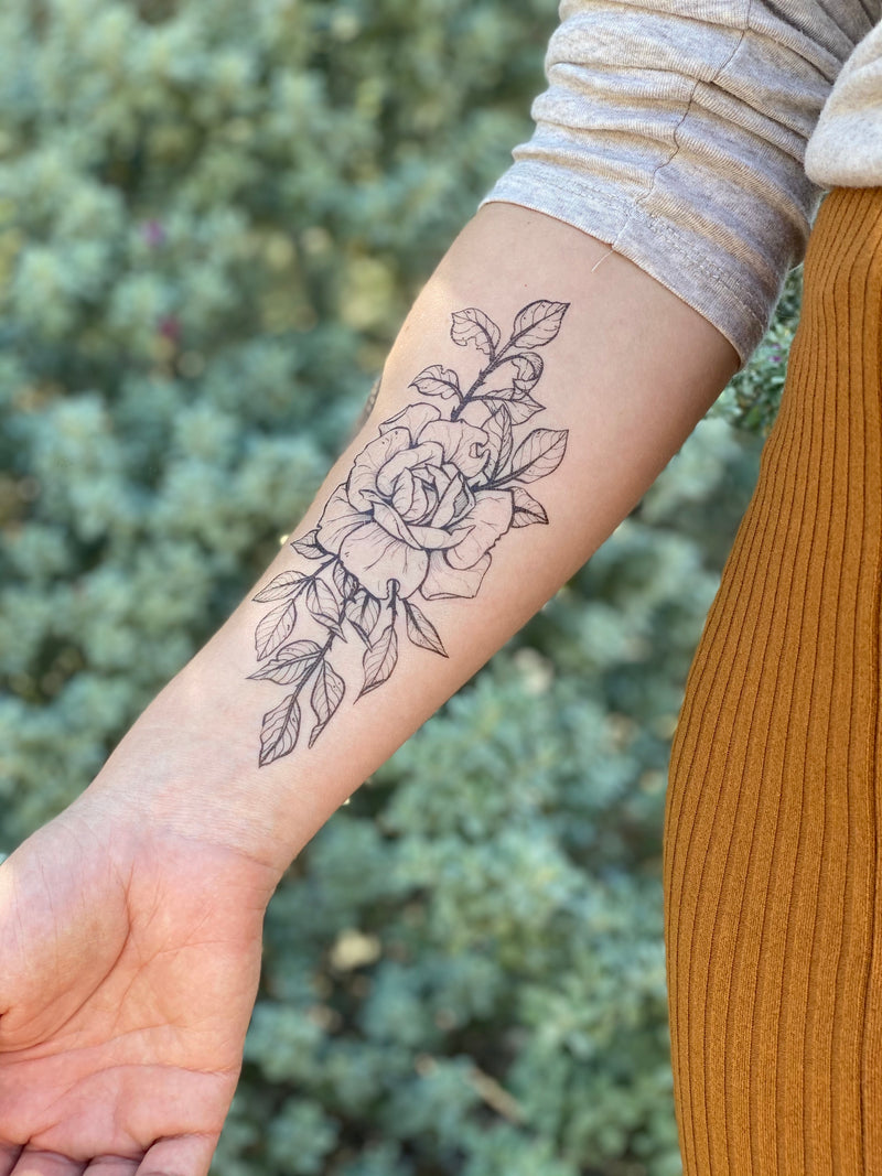 Rose temporary tattoo on persons arm wearing orange and white in a green blurred background 