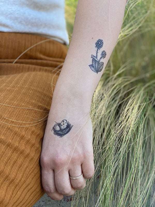 forest forage temporary tattoo split up onto hand and forearm on a person wearing orange and white with a background of wispy leaves that are green 