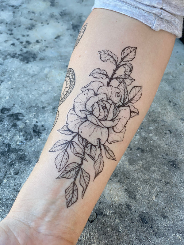 rose temporary tattoo on persons arm with a grey background 
