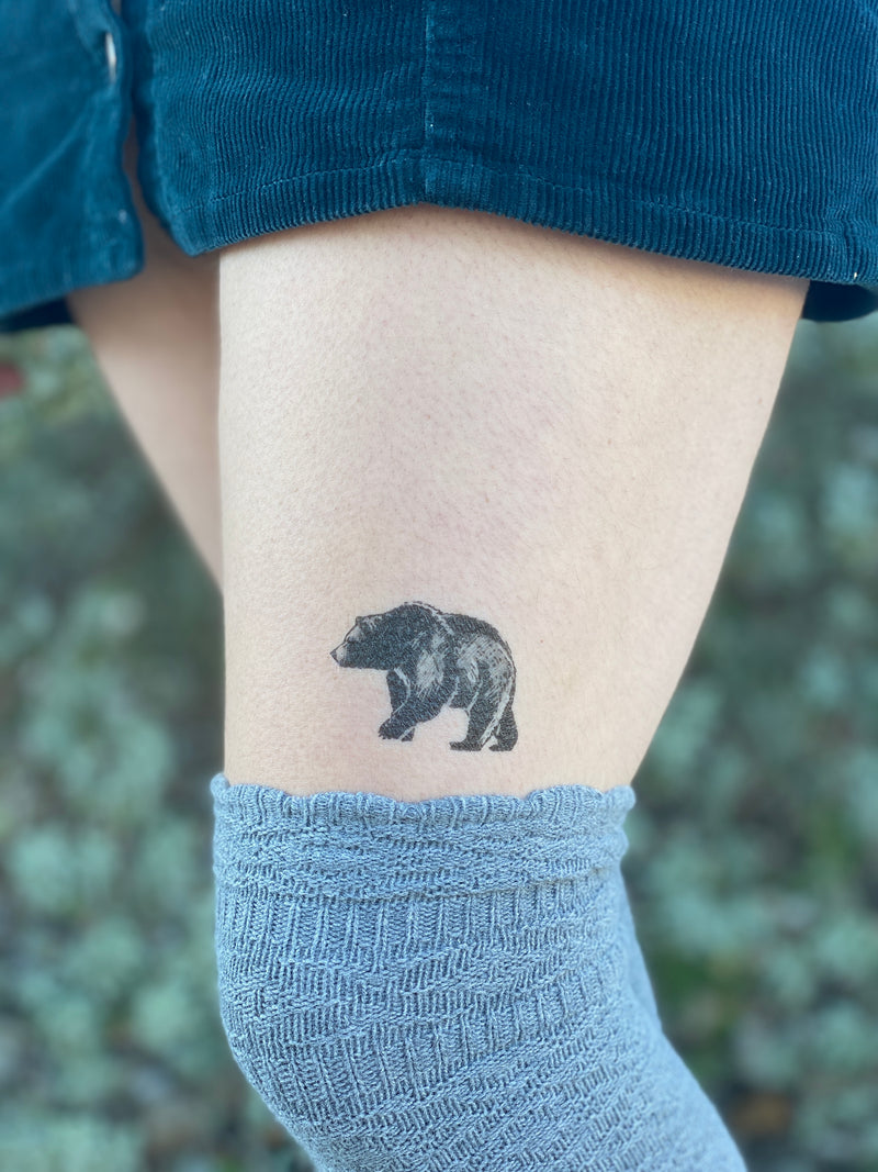 bear temporary tattoo above knee with a grey and blue clothes and a blurred green background 