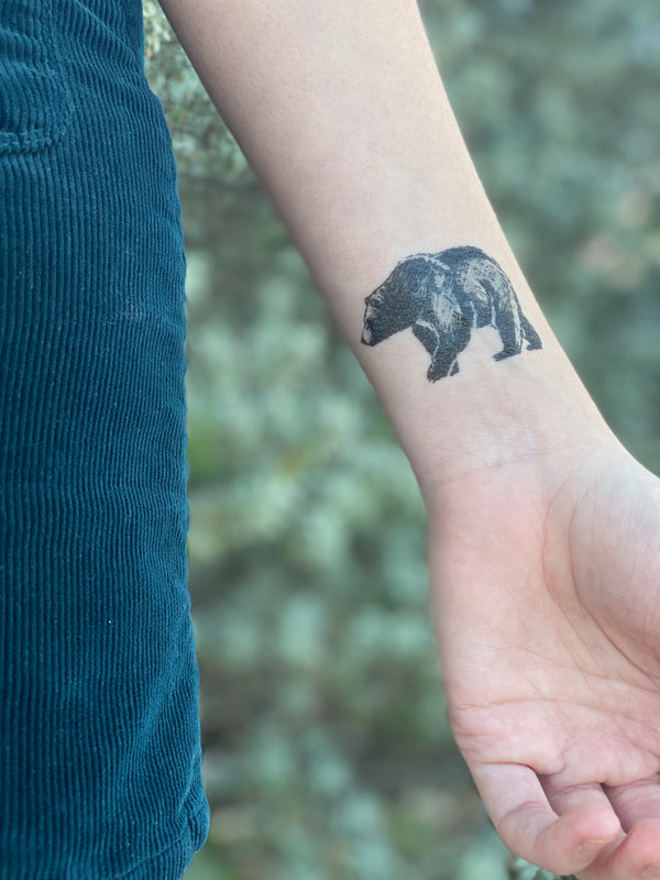 small bear temporary tattoo on wrist of a person wearing blue in a background of blurred green nature 