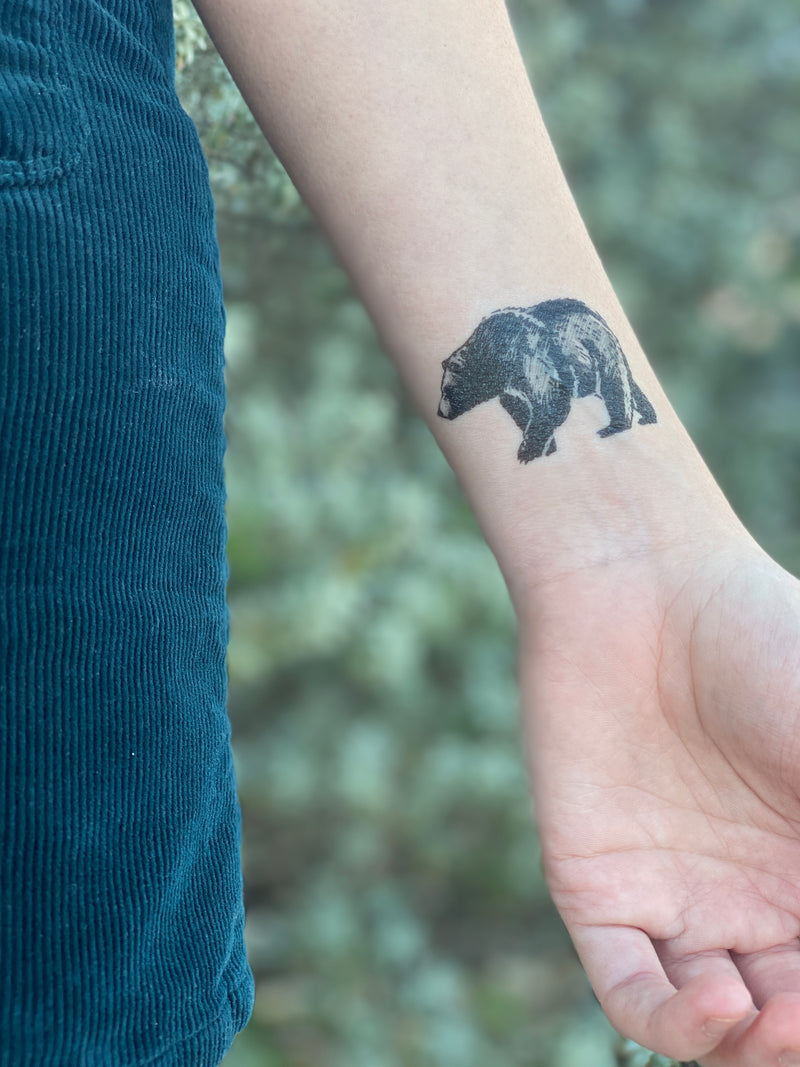 small bear temporary tattoo on wrist of a person wearing blue in a background of blurred green nature 
