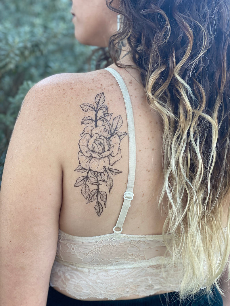 Rose temporary tattoo on persons back wearing white in a green blurred nature background 