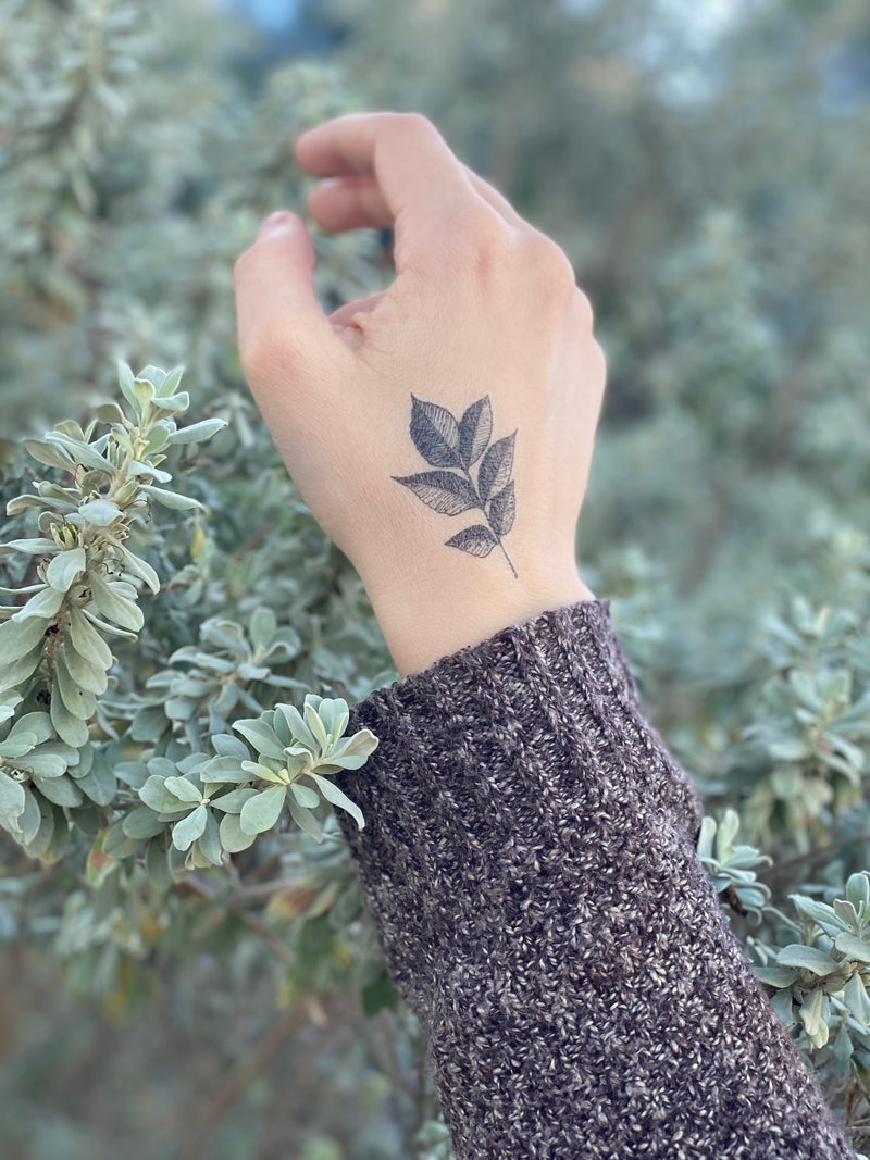 leaf temporary tattoo on hand of a person wearing a grey sweater in a background of green leaves 