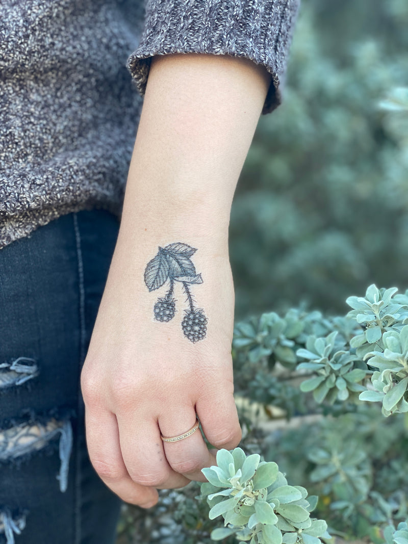floral temporary tattoo on hand with a grey sweater and blue pants, with a leafy green background 