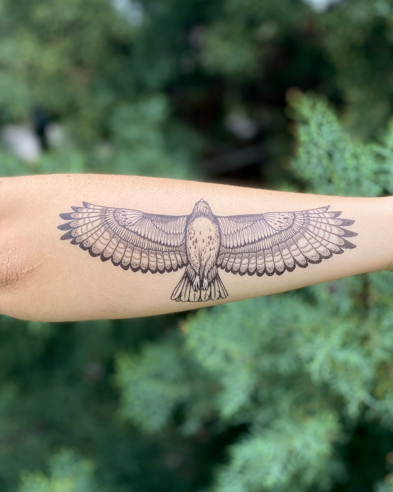A temporary tattoo of a black and white hawk in flight, applied on a person's forearm.